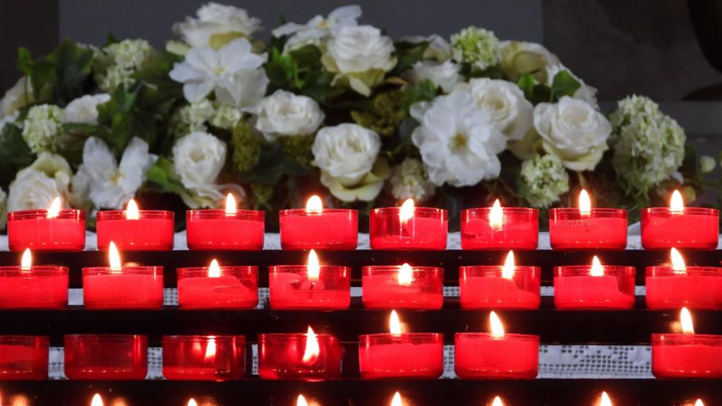 Ein ruhiges Arrangement aus brennenden roten Kerzen mit weißen Blumen im Hintergrund, das eine friedvolle Atmosphäre schafft.